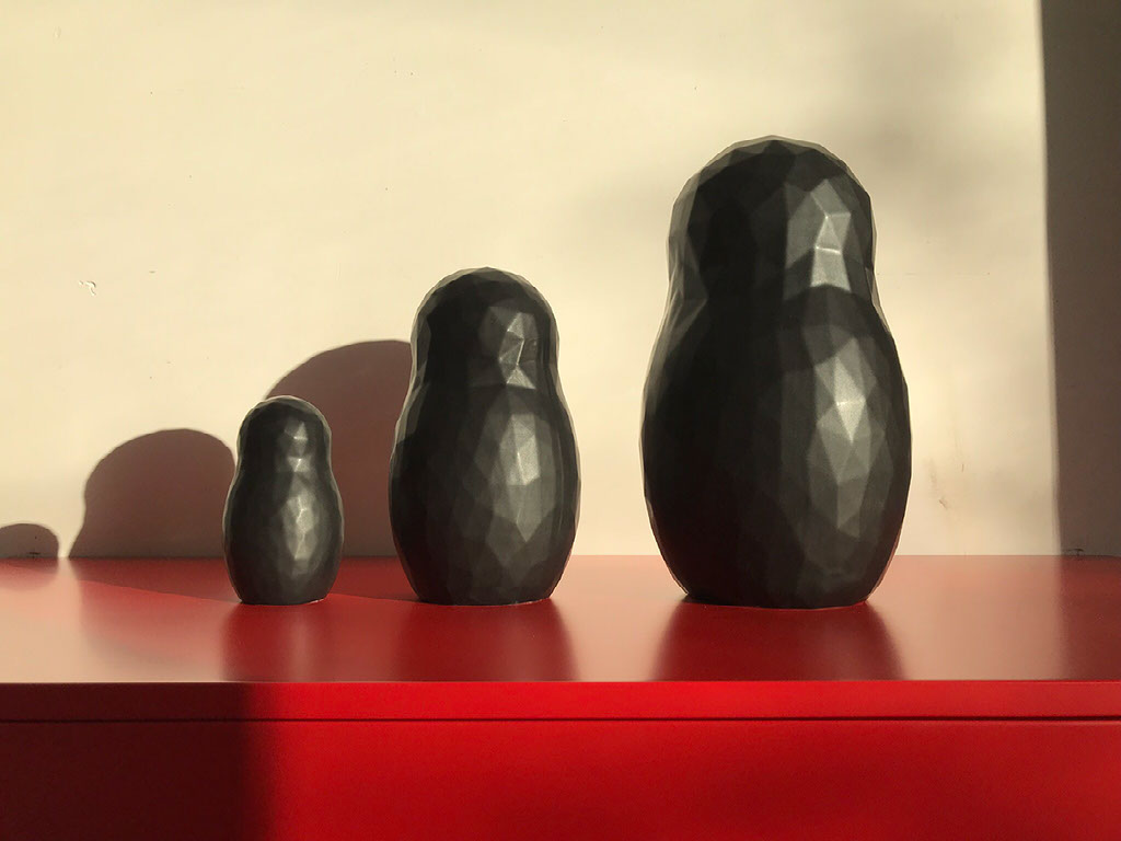 Matroesjka trio — three sizes in faceted charcoal on a red lacquer ledge